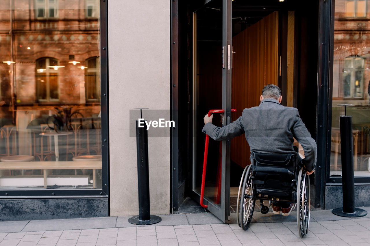 Rear view of disabled mature man sitting on wheelchair while entering in store