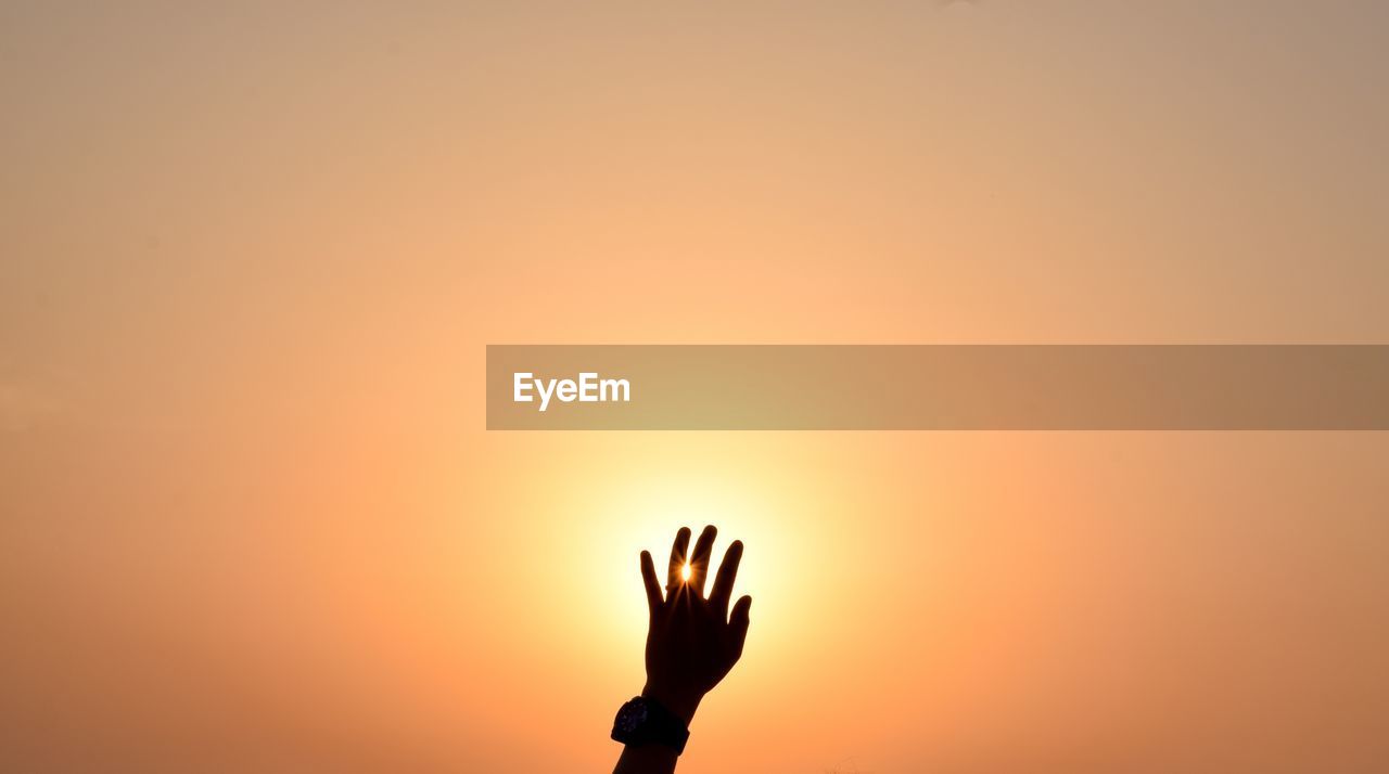 Silhouette person hand against orange sky during sunset