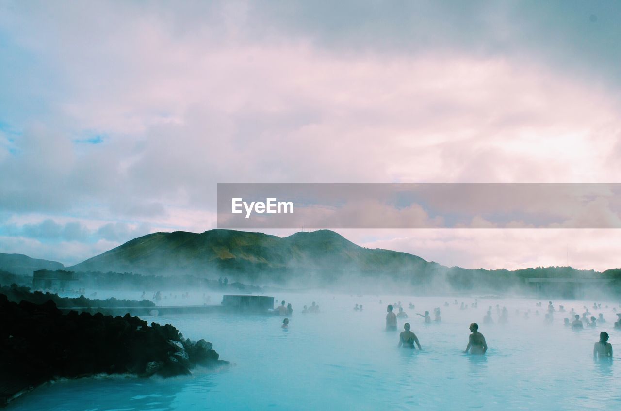 Crowd bathing in hot spring against cloudy sky