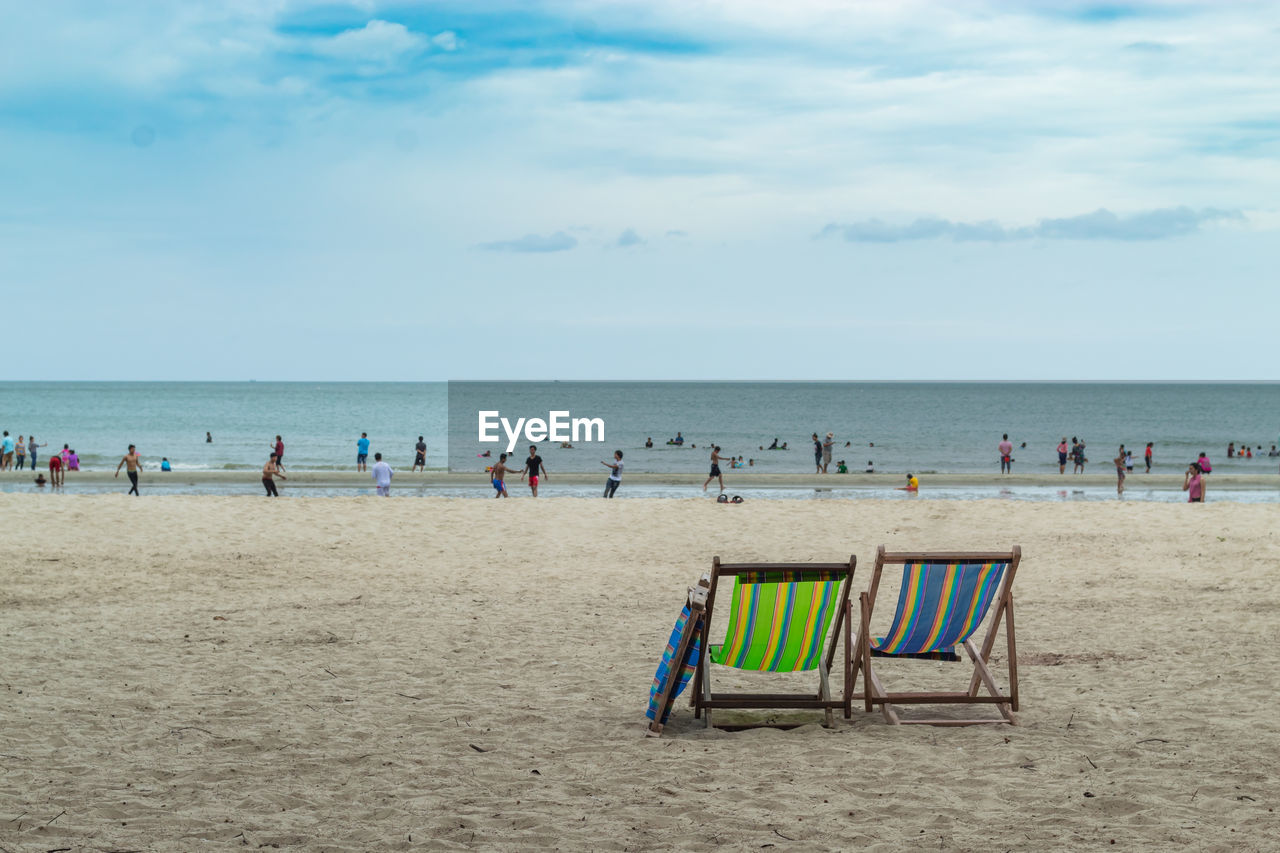 Empty chairs with people in background at beach