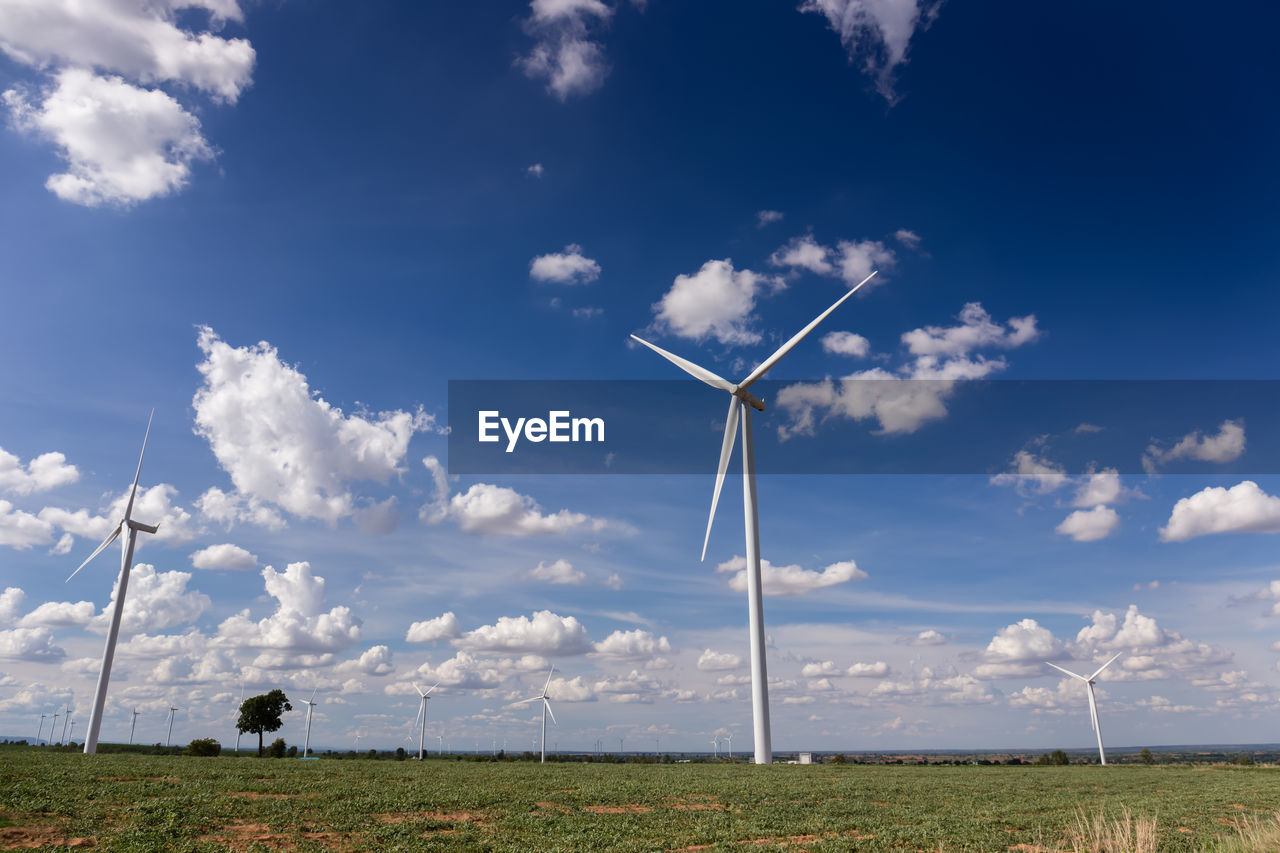 Low angle view of windmills on field against cloudy sky