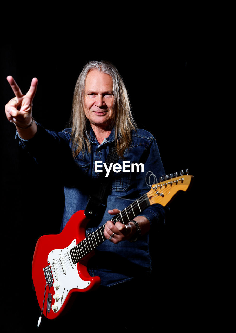 music, musical instrument, musician, guitar, one person, string instrument, arts culture and entertainment, black background, musical equipment, performance, electric guitar, studio shot, adult, concert, bass guitar, indoors, plucking an instrument, performing arts, blond hair, rock music, long hair, singing, front view, person, enjoyment, portrait, plucked string instruments, women, happiness, emotion, hairstyle, smiling, entertainment, copy space, skill, black, casual clothing, stage, cheerful, vitality, mouth open, holding