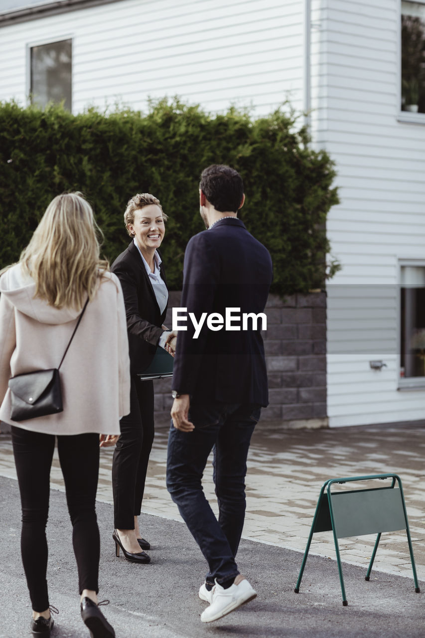 Smiling real estate professional greeting couple outside new house