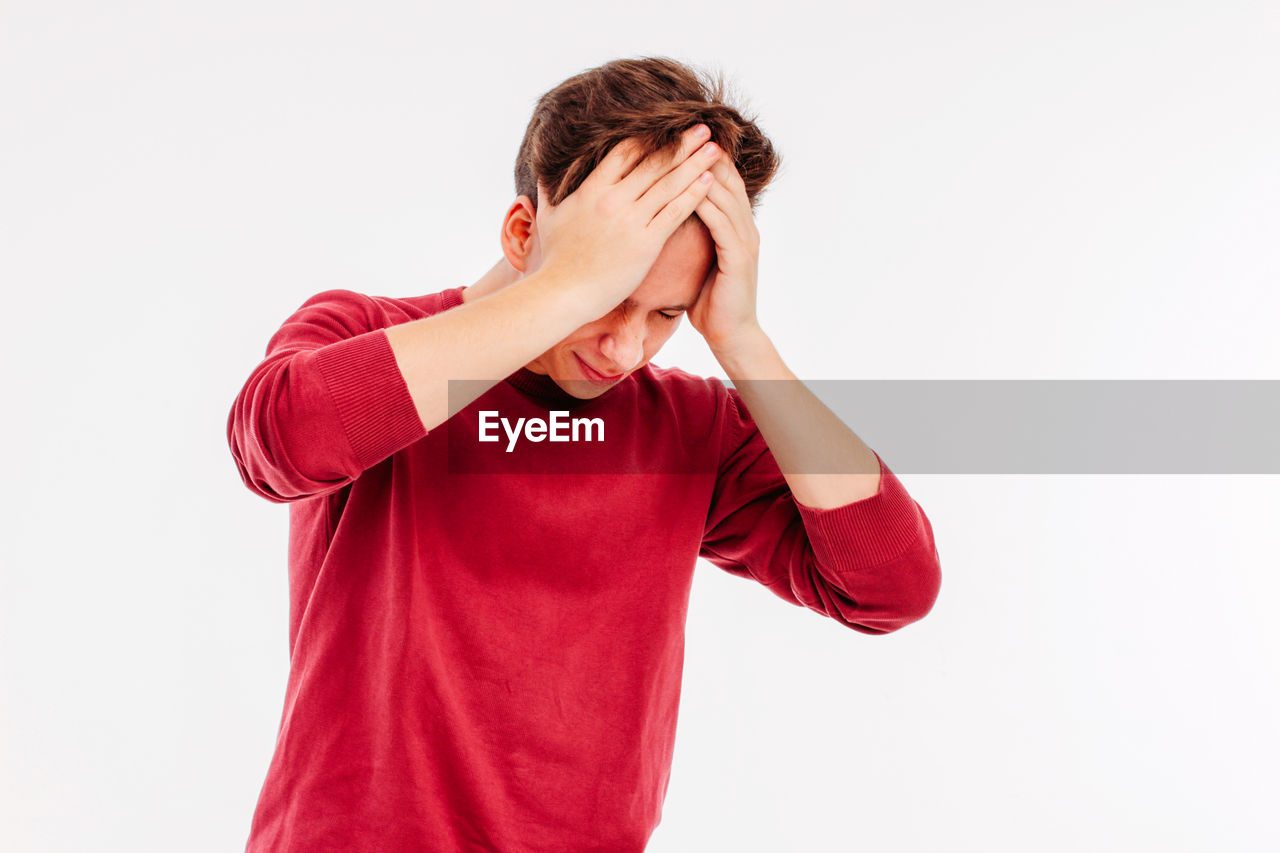 Young man with head in hands while standing against white background