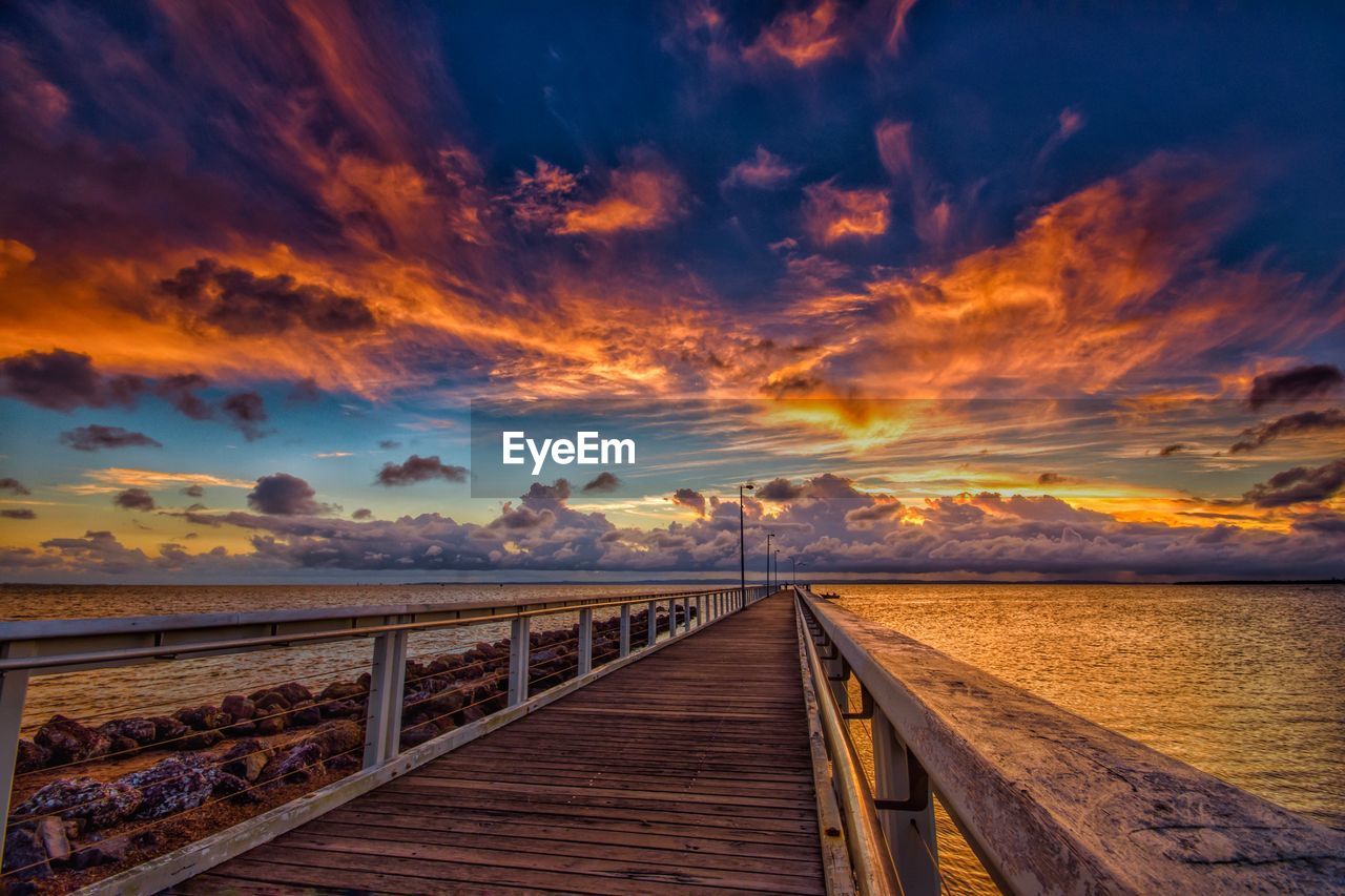 Scenic view of empty pier over sea during sunset