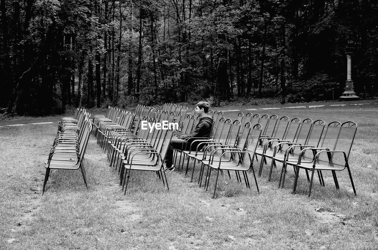 Boy sitting on chair at field in forest