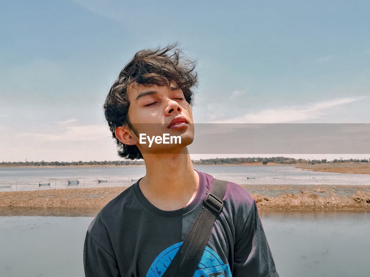 Portrait of teenage boy closing his eyes against sky