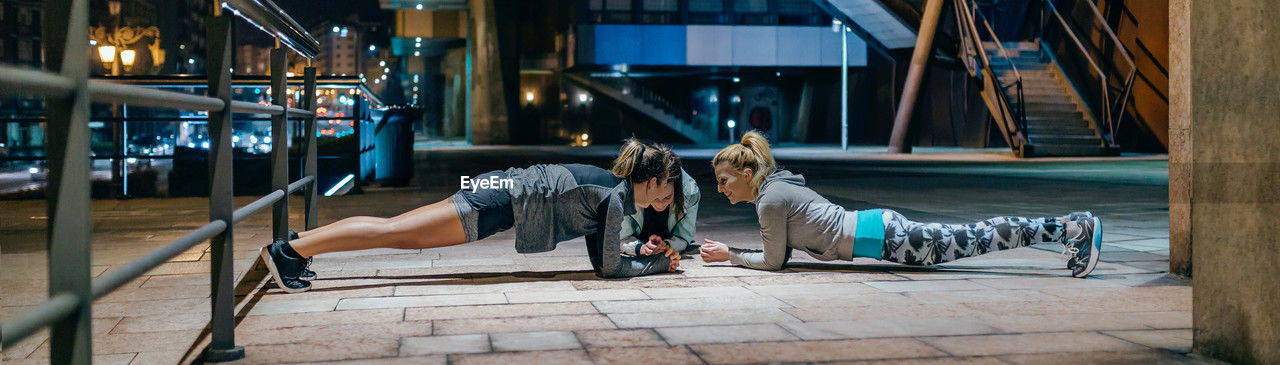 Women sport team doing plank exercise during training on the city at night