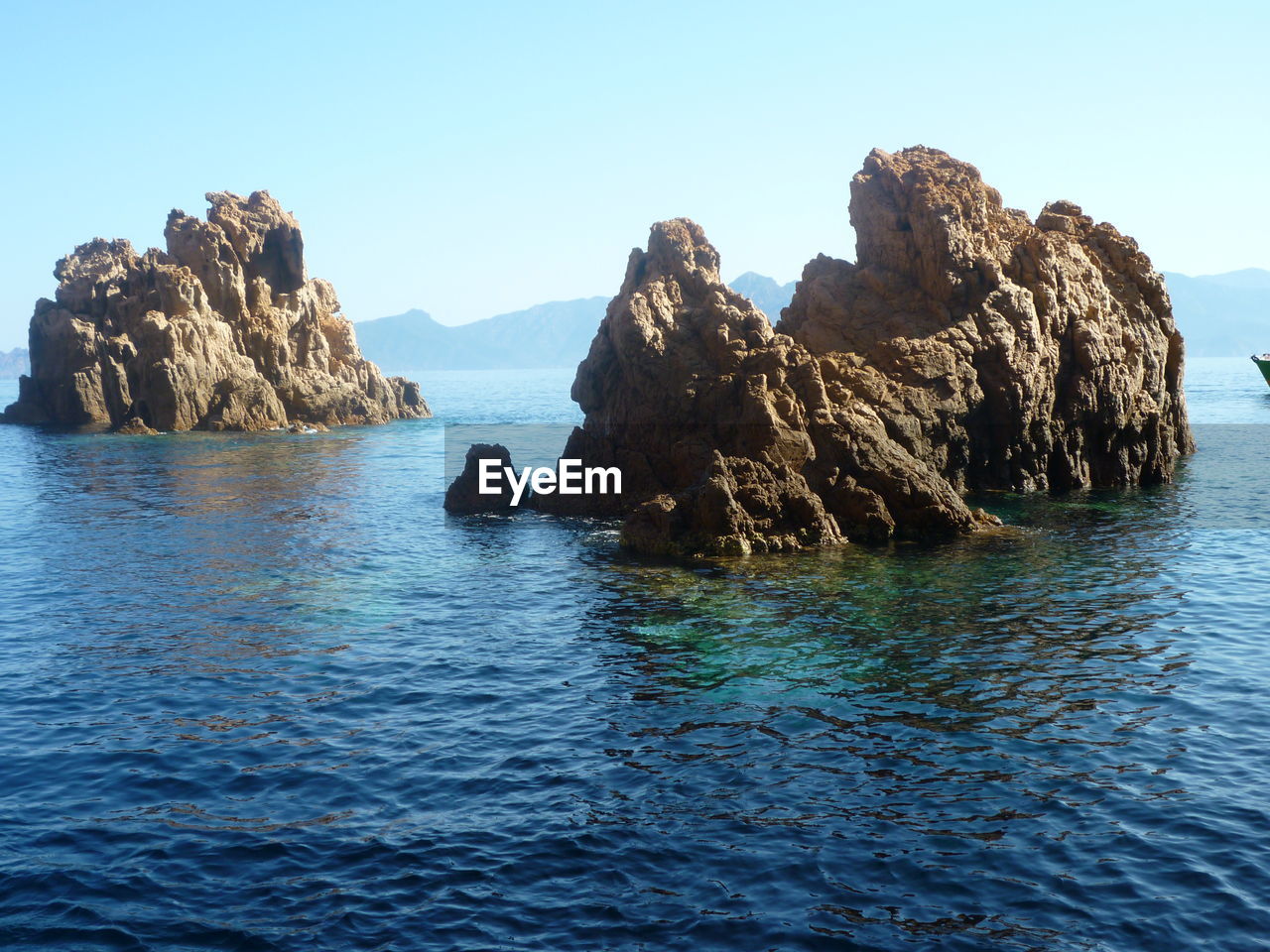 Rock formation in sea against clear blue sky