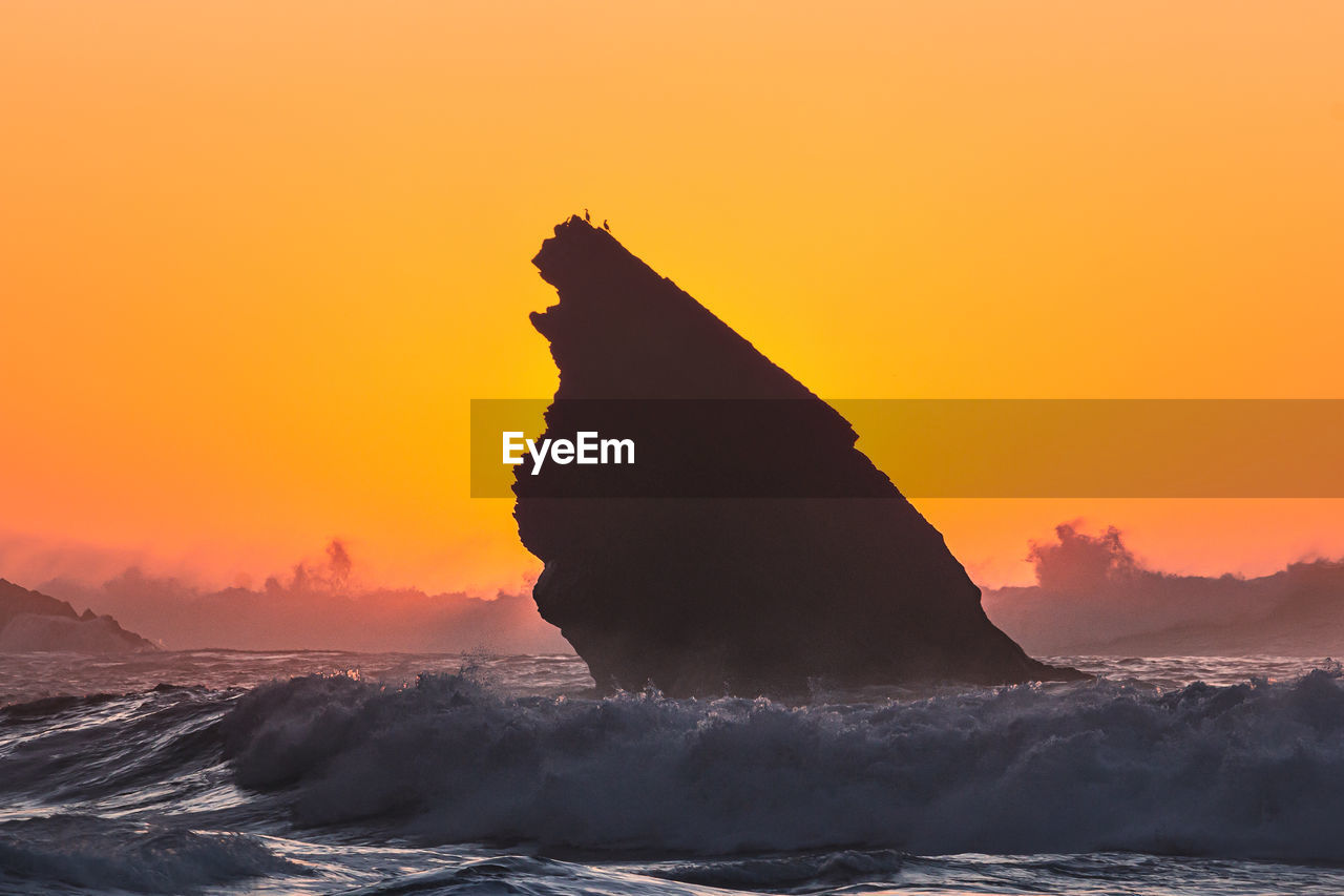 Silhouette rock on beach against sky during sunset
