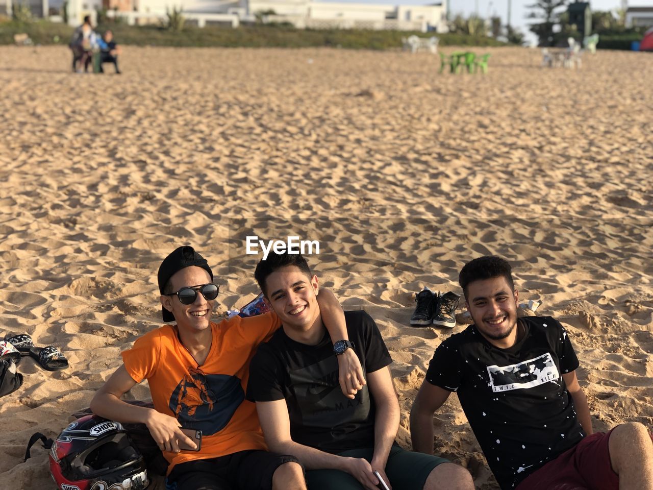 PORTRAIT OF SMILING YOUNG PEOPLE SITTING ON BEACH