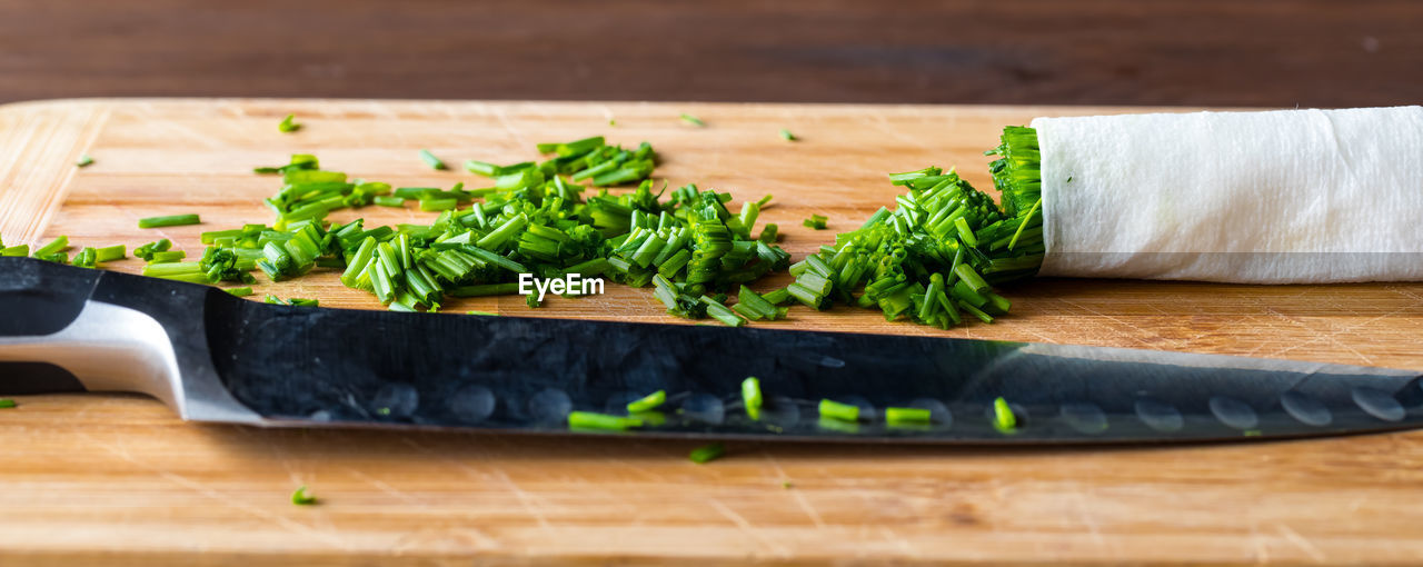 A narrow view of a pile of chopped chives with a sharp knife in front.