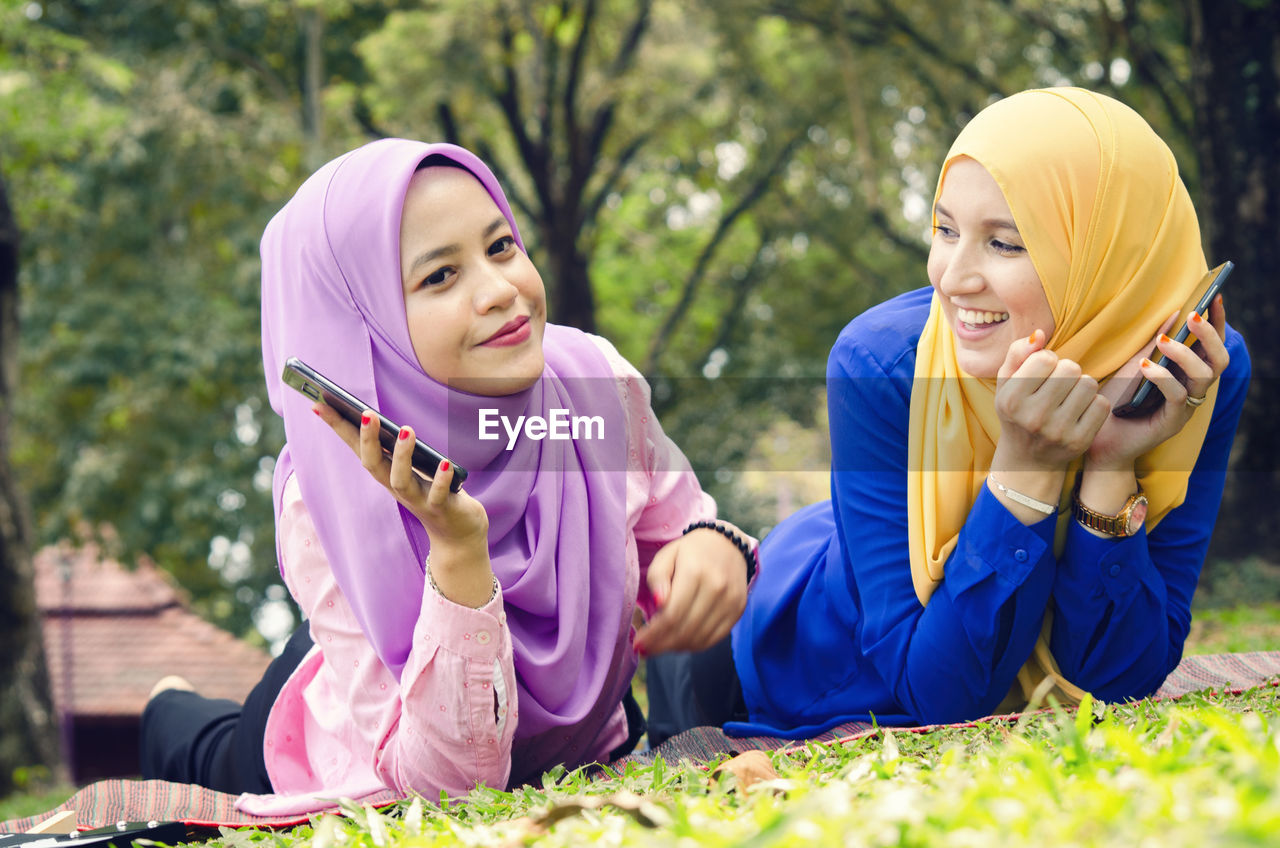  friendship and happiness concept. portrait of smile young muslimah laying on grass at city park