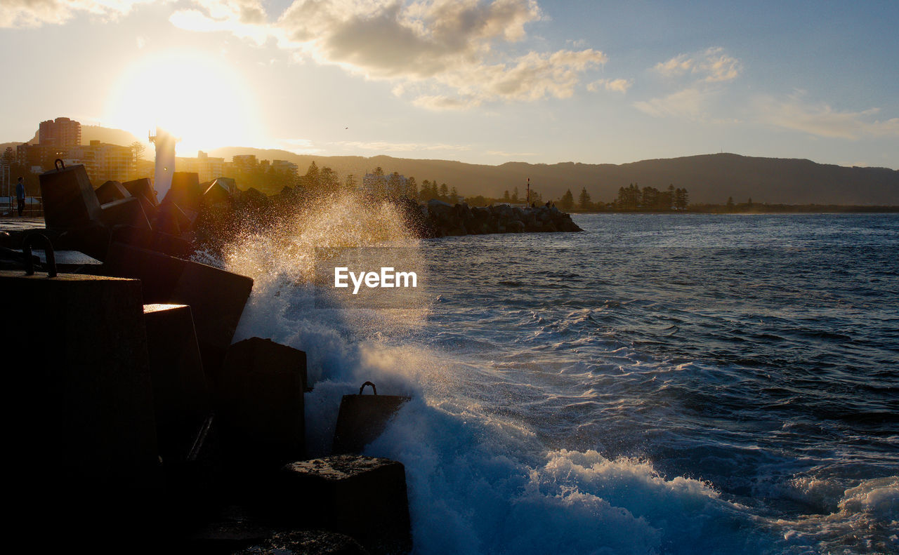 Water splashing in sea against sky during sunset