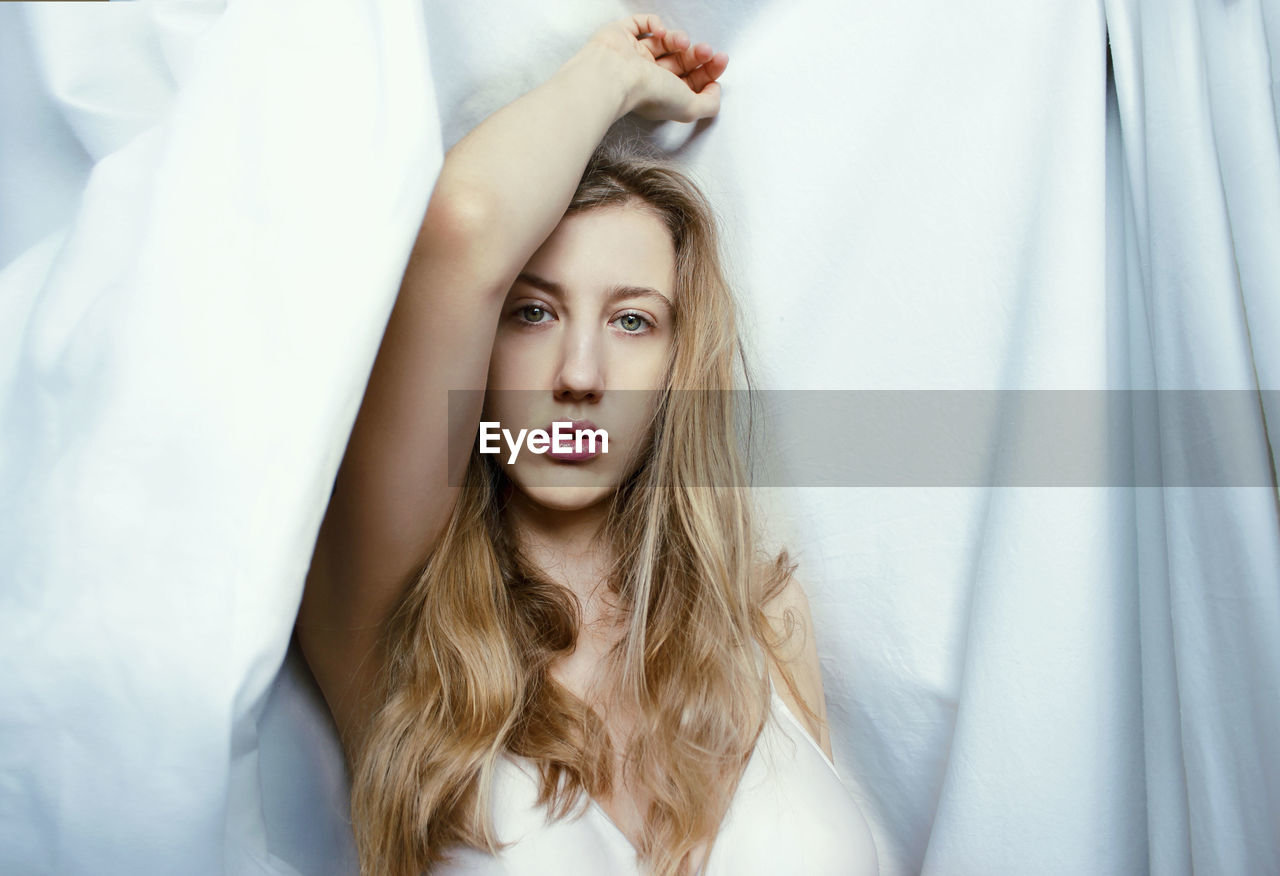 Portrait of young woman with long hair by curtain