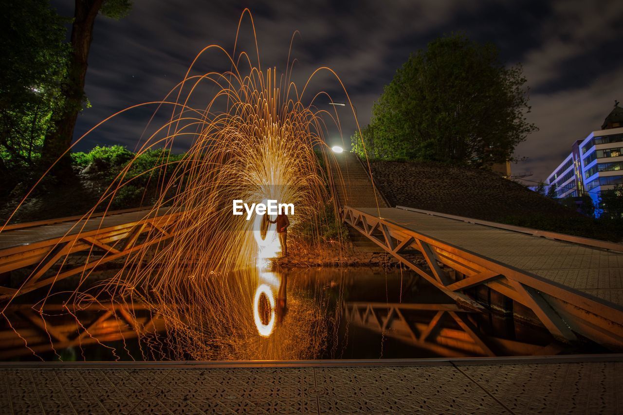 Reflection of man standing by wire wool in lake at night