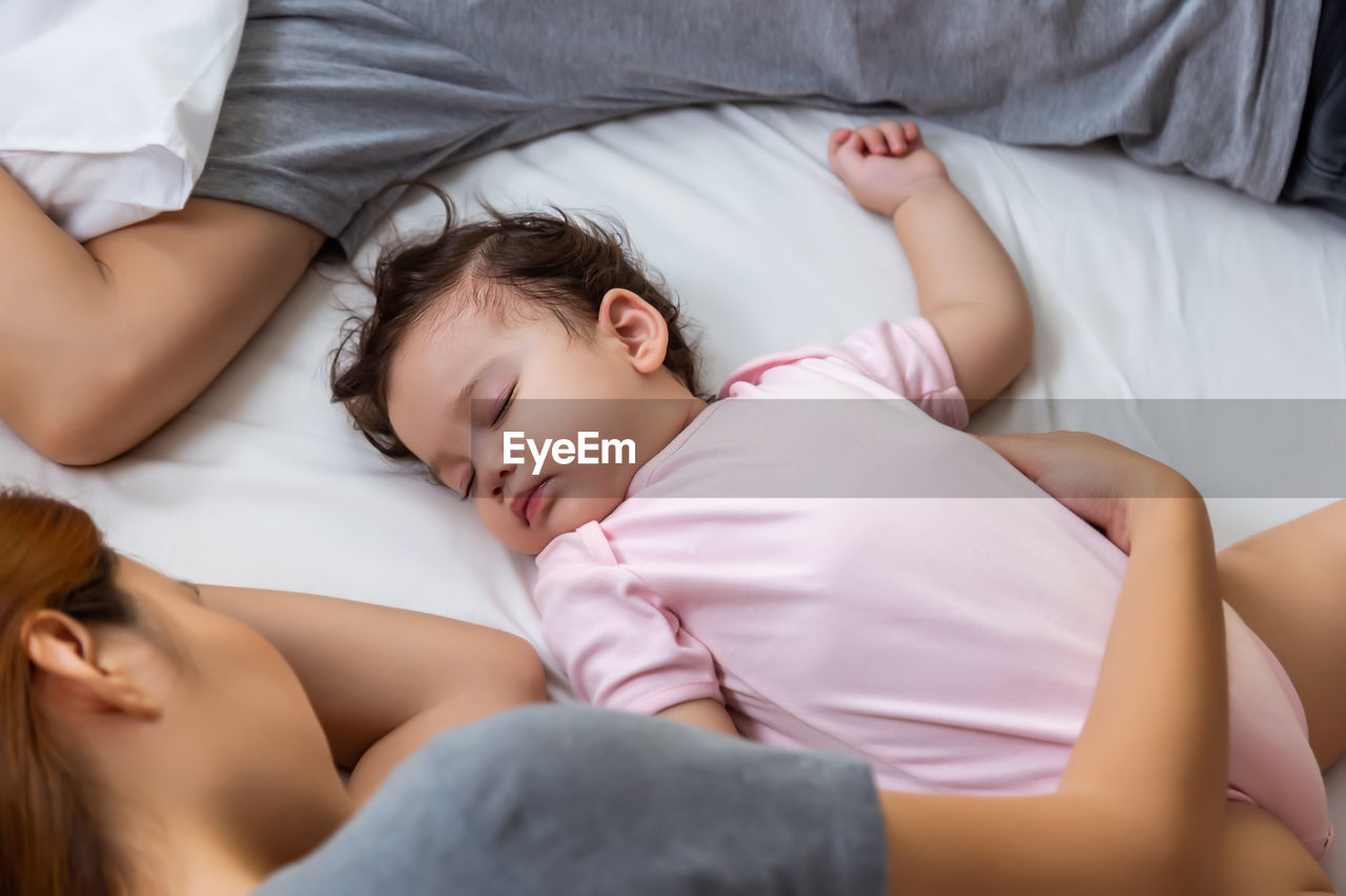 High angle view of baby sleeping on bed with parent at home