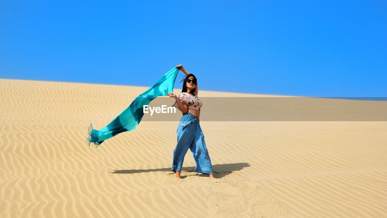 Full length of young woman holding scarf at desert on sunny day