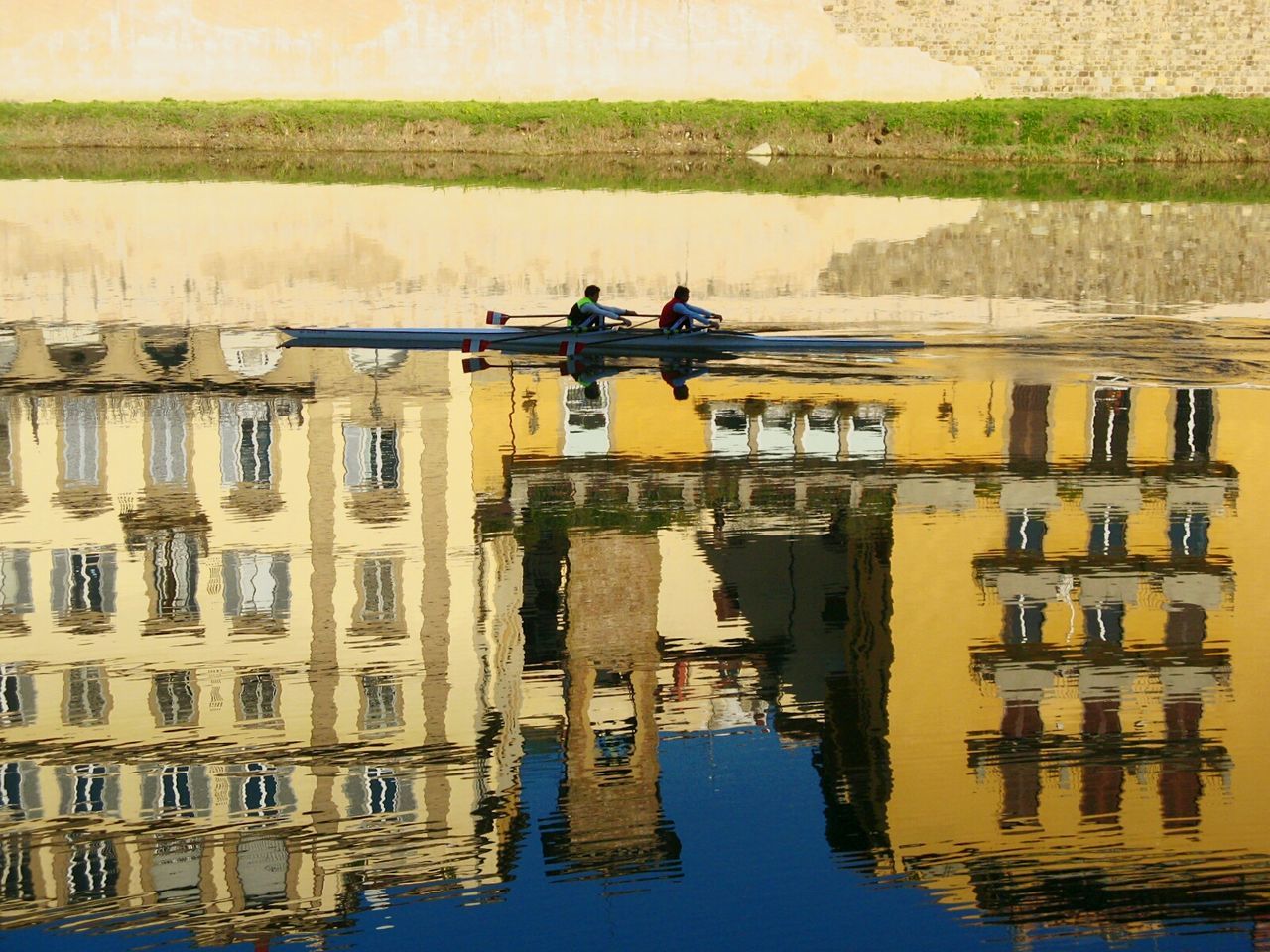 Men rowing on river with reflection of buildings