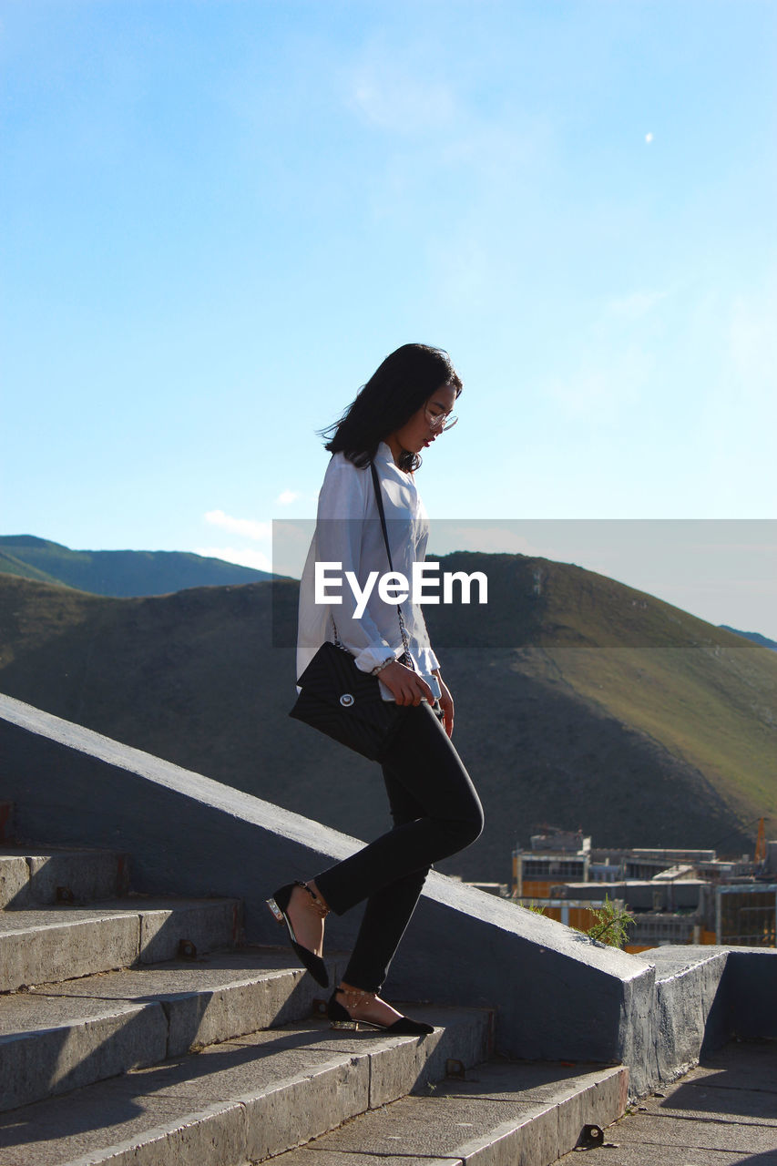 SIDE VIEW OF WOMAN STANDING AGAINST MOUNTAIN