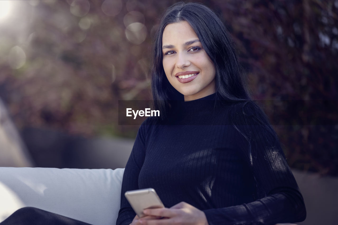 Portrait of smiling young woman using mobile phone outdoors