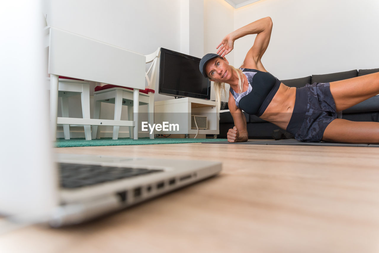 Strong female athlete in sportswear doing side plank exercise while smiling and training at home