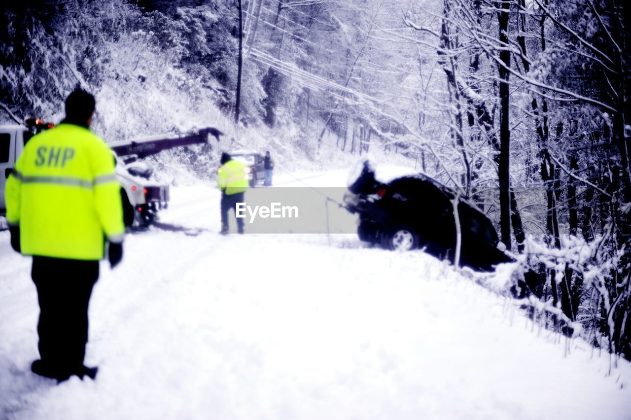 Rescuers pulling fallen car on snow covered road against bare trees