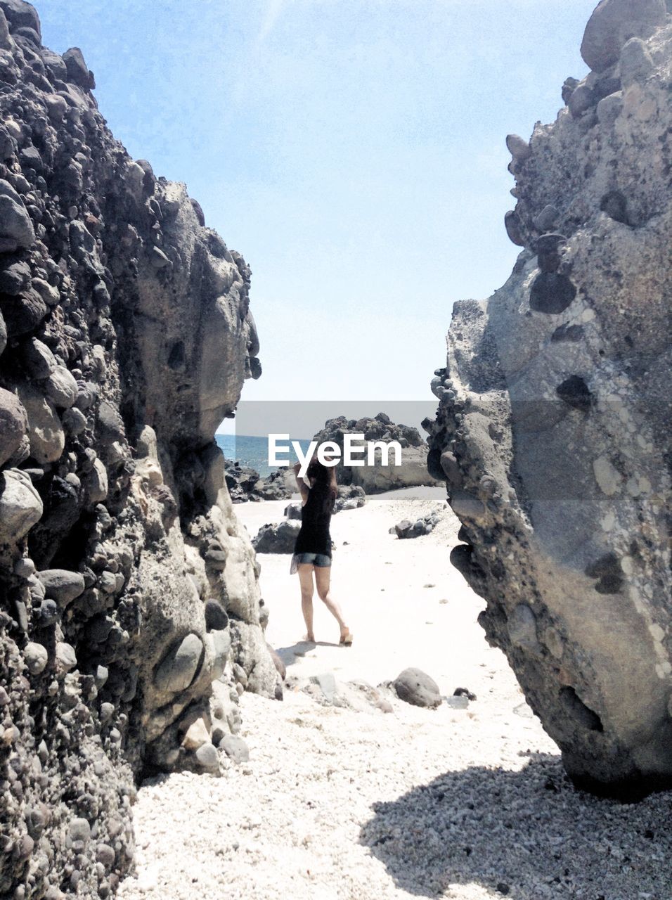 Rear view of woman standing at beach against clear sky