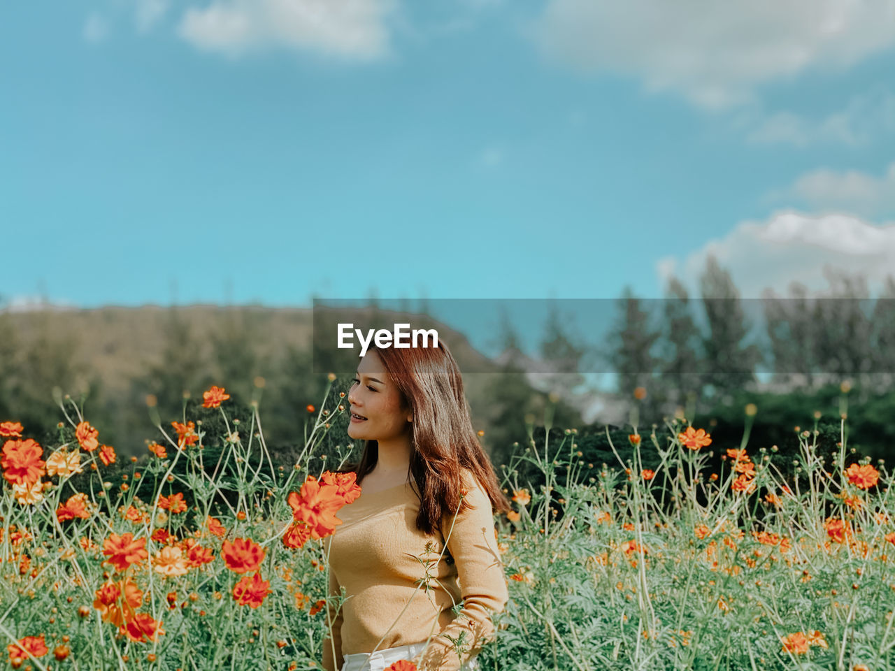 Beautiful woman standing in field with flowers against sky