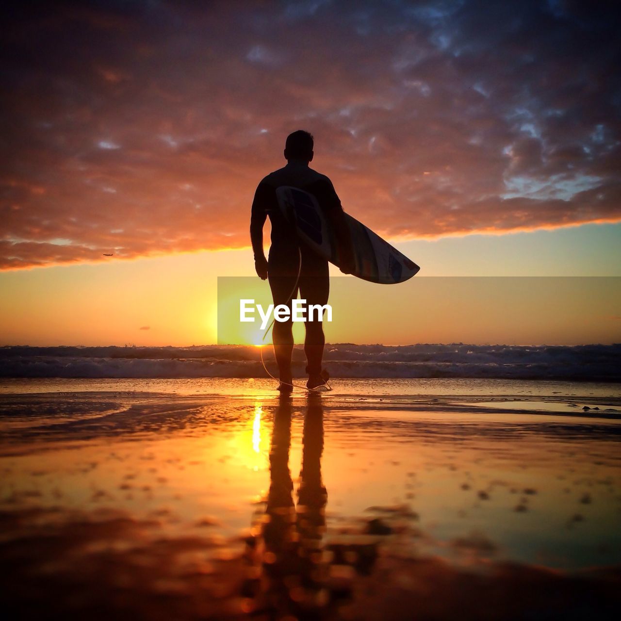 Silhouette man carrying surfboard on beach at sunset