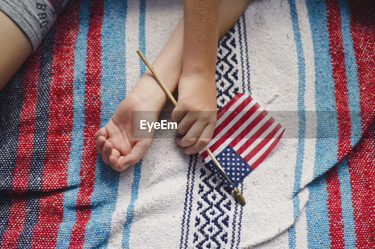 High angle view of hand holding american flag while lying on bed