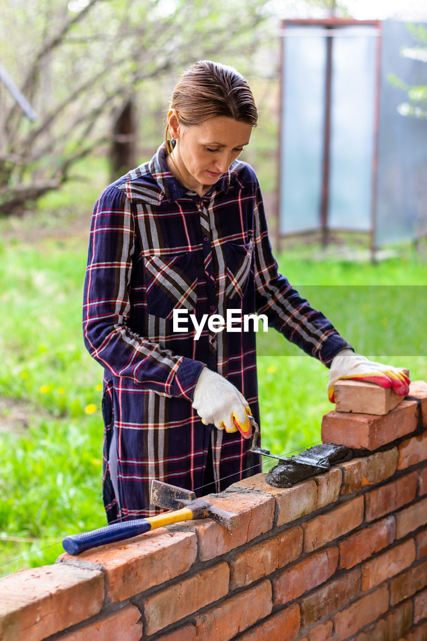 Young woman bricklayer lay out cement mortar for brickwork with a trowel on a brick wall