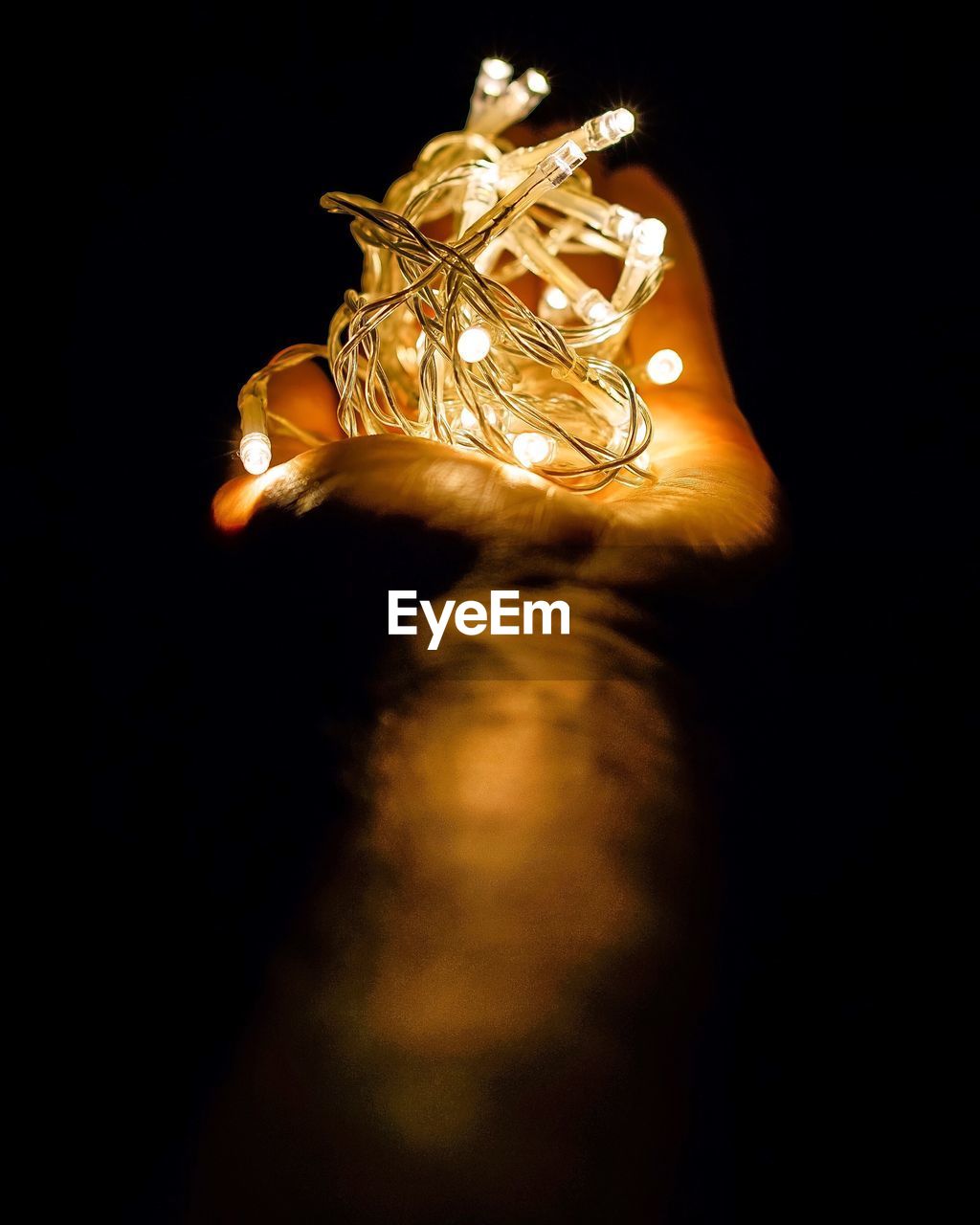 Close-up of hand holding illuminated string light against black background