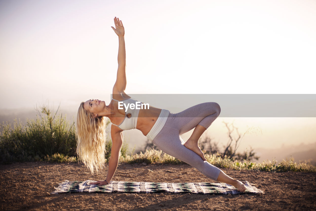 Smiling woman doing yoga on field against clear sky