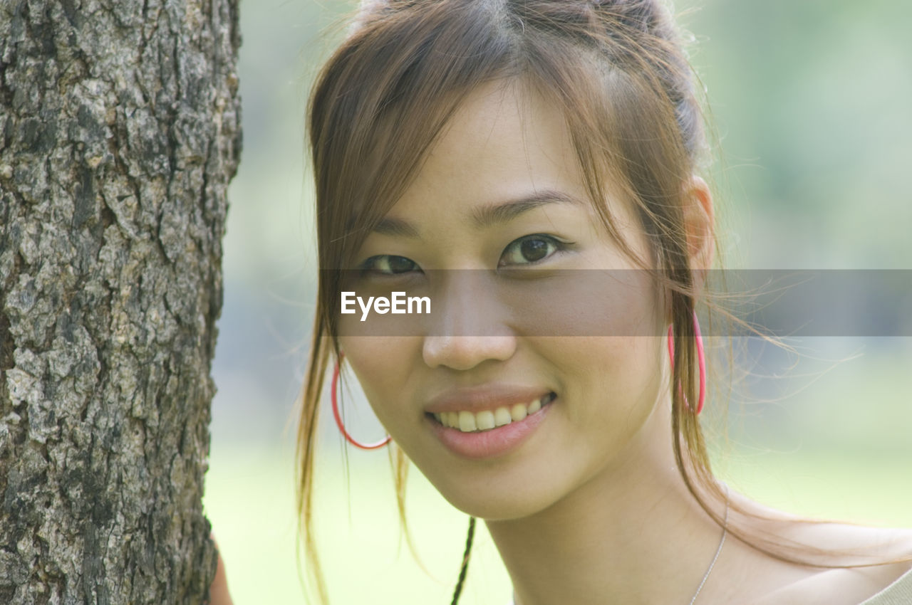 Portrait of beautiful woman by tree trunk in park