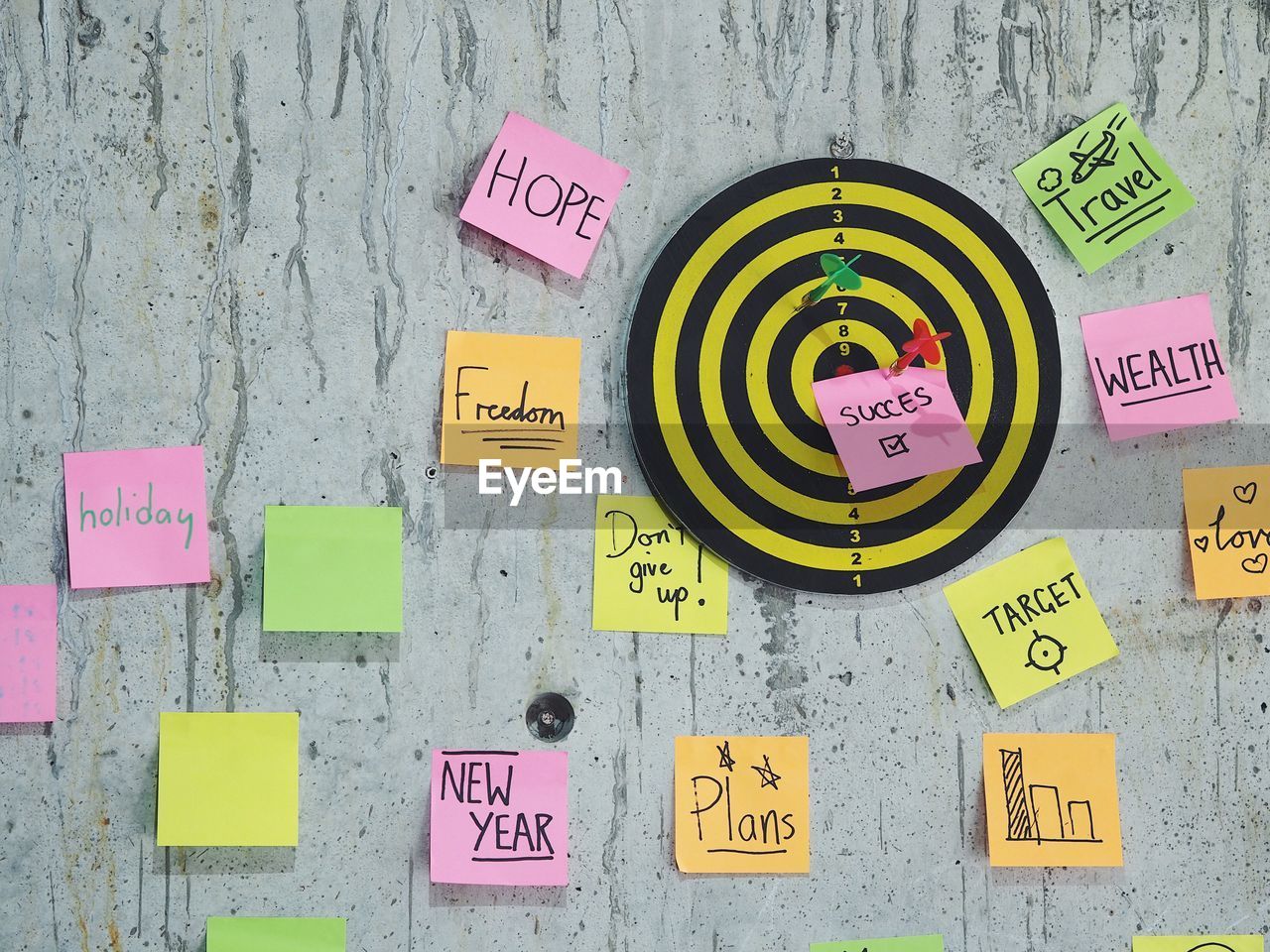 Close-up of dart on dartboard with adhesive notes against wall