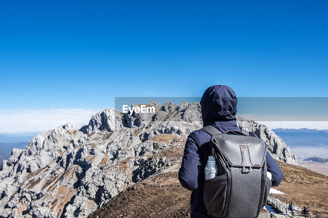 REAR VIEW OF MAN AGAINST BLUE SKY AND MOUNTAIN