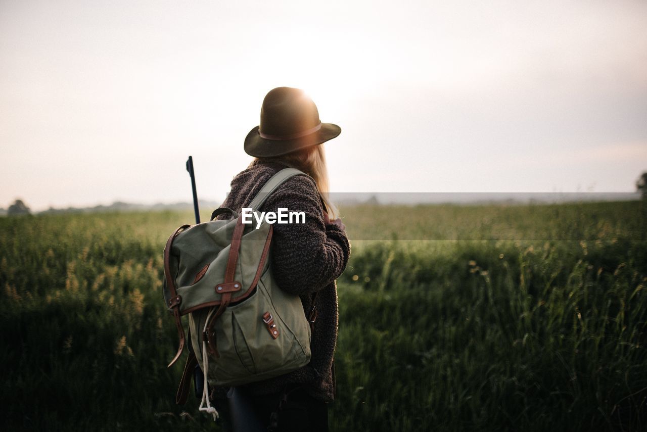 Side view of woman with backpack standing on land against sky at sunset