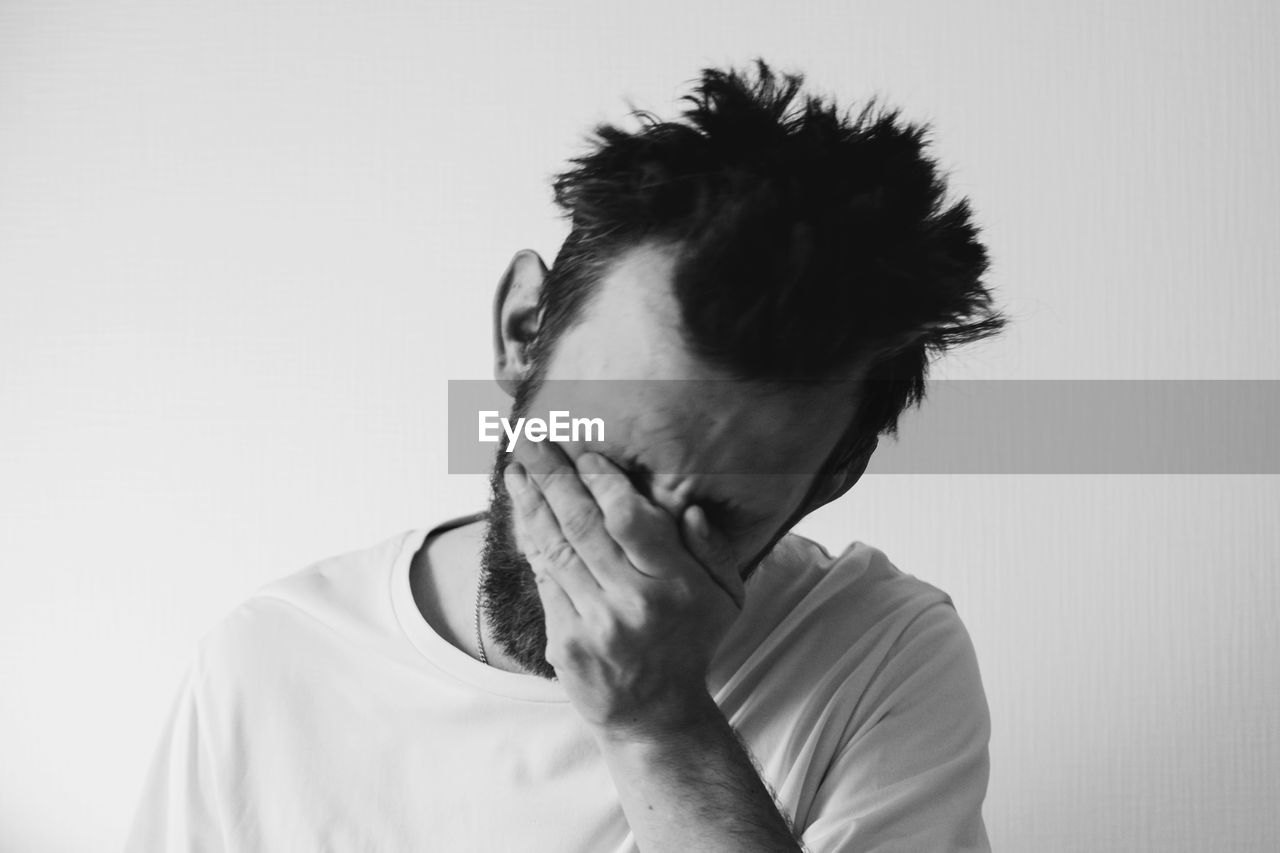 PORTRAIT OF YOUNG MAN WITH EYES CLOSED AGAINST WHITE BACKGROUND