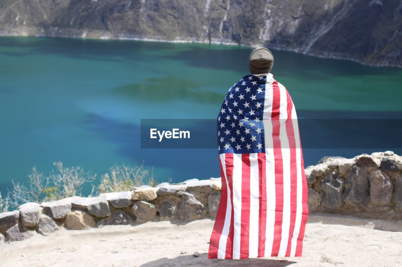 Rear view of man with american flag standing by lake