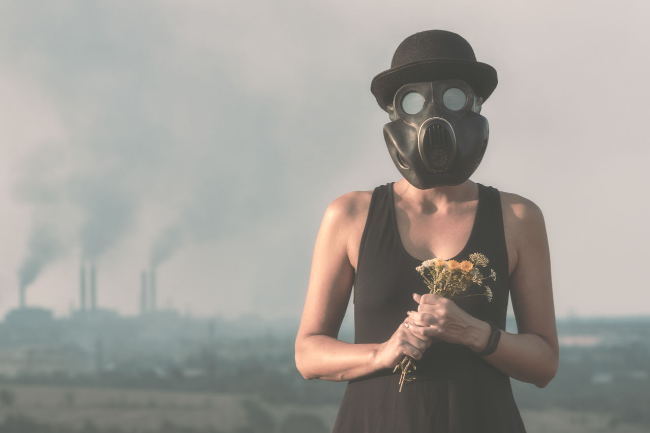 Woman wearing gas mask holding flowers while standing outdoors