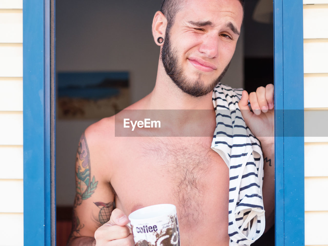 Close-up portrait of man winking while having coffee standing at doorway