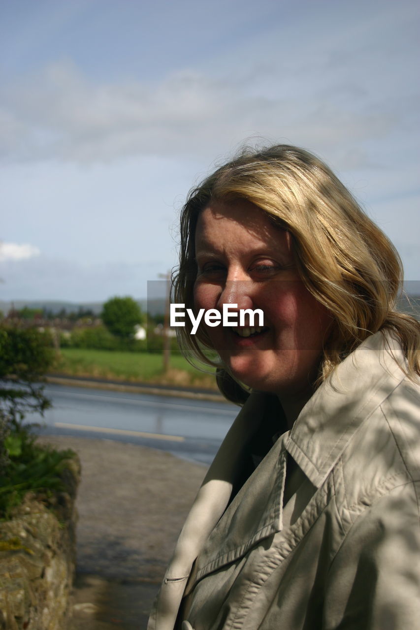 PORTRAIT OF SMILING WOMAN AGAINST WATER