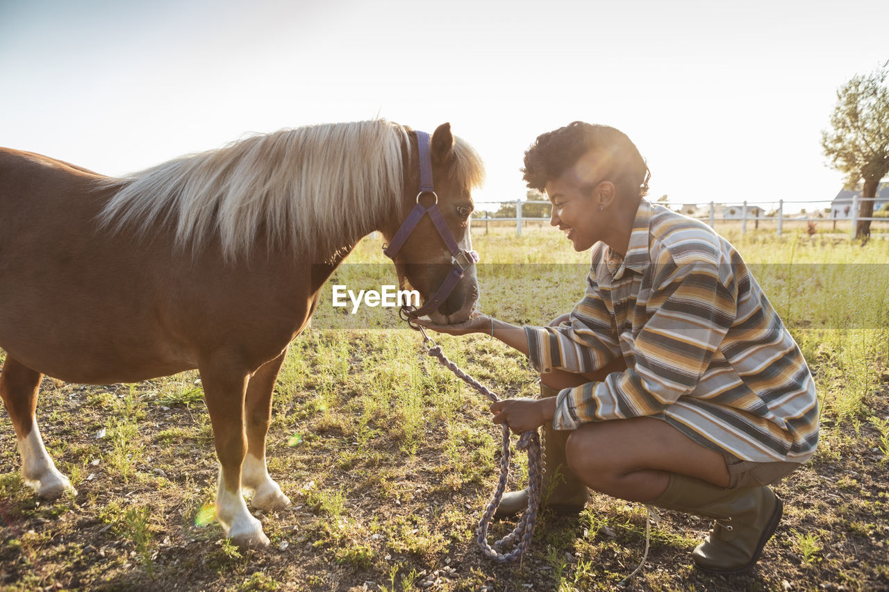 Smiling female farm worker feeding pony at farm