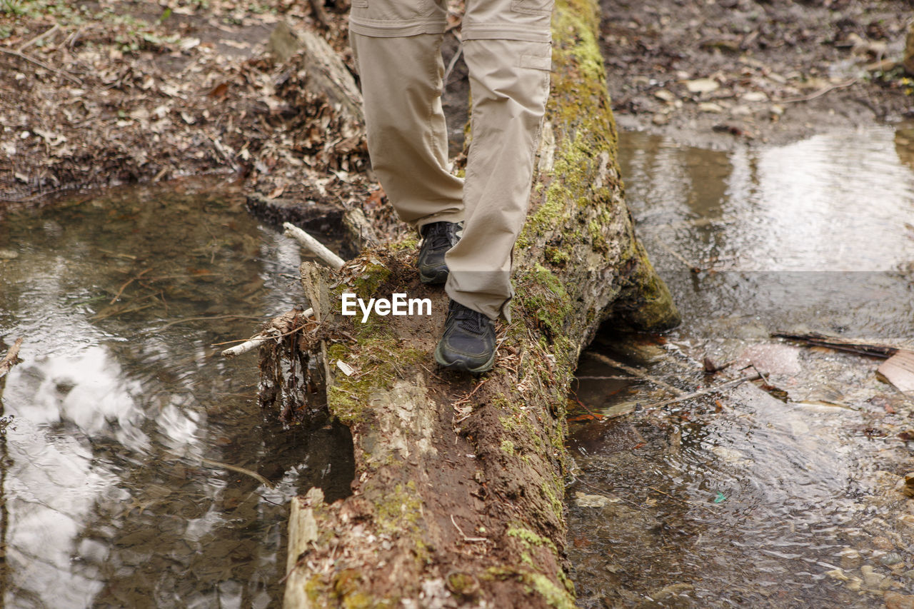 Bottom-half of a man crossing a creek on moss-covered log in nature