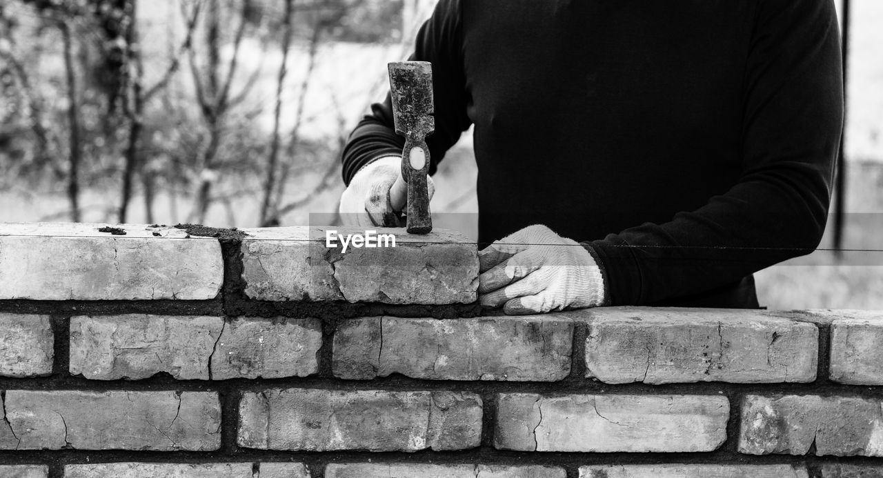 A man builds a wall of bricks, lays a brick on a cement-sand mortar, tapping a brick with a hammer
