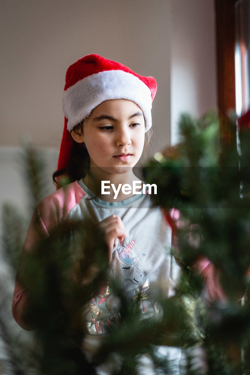 Girl wearing santa hat decorating christmas tree at home