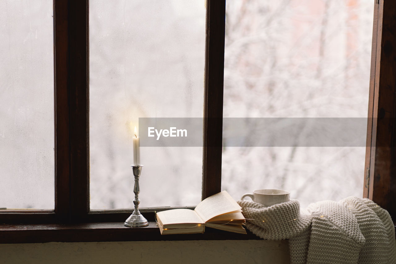 Cup of hot tea and an open book with a warm sweater on a vintage wooden windowsill