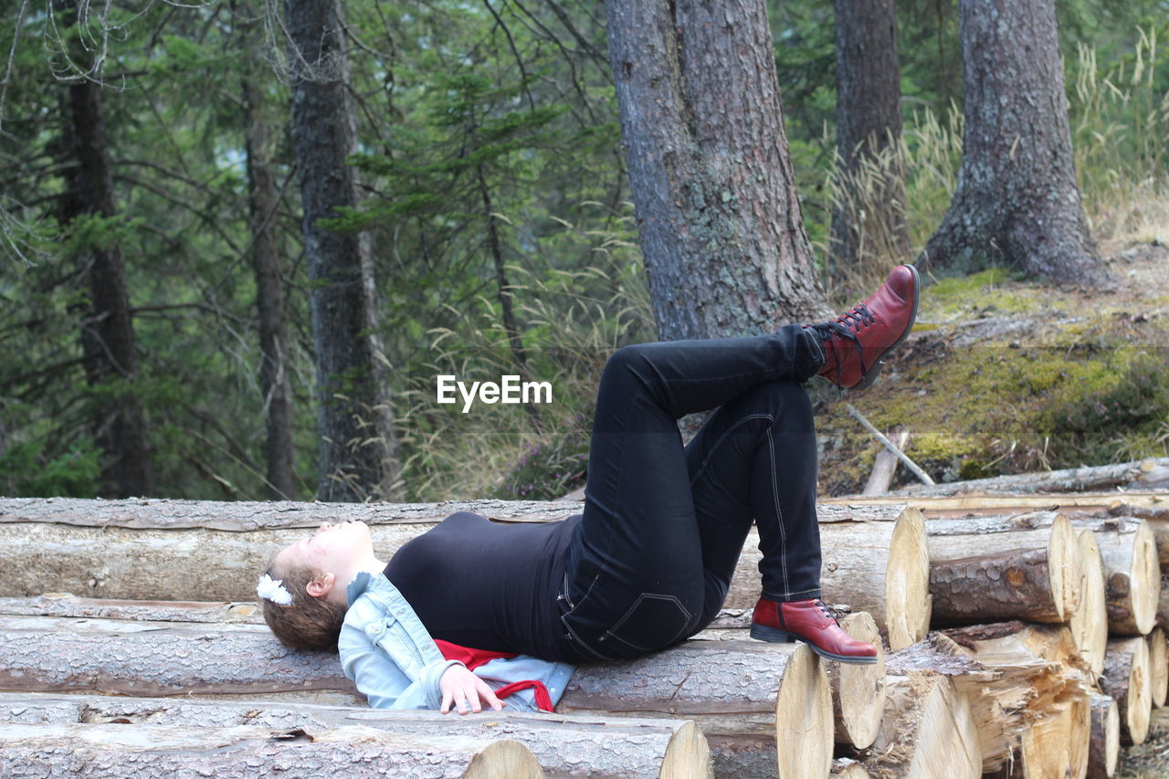 Side view of woman relaxing on logs in forest