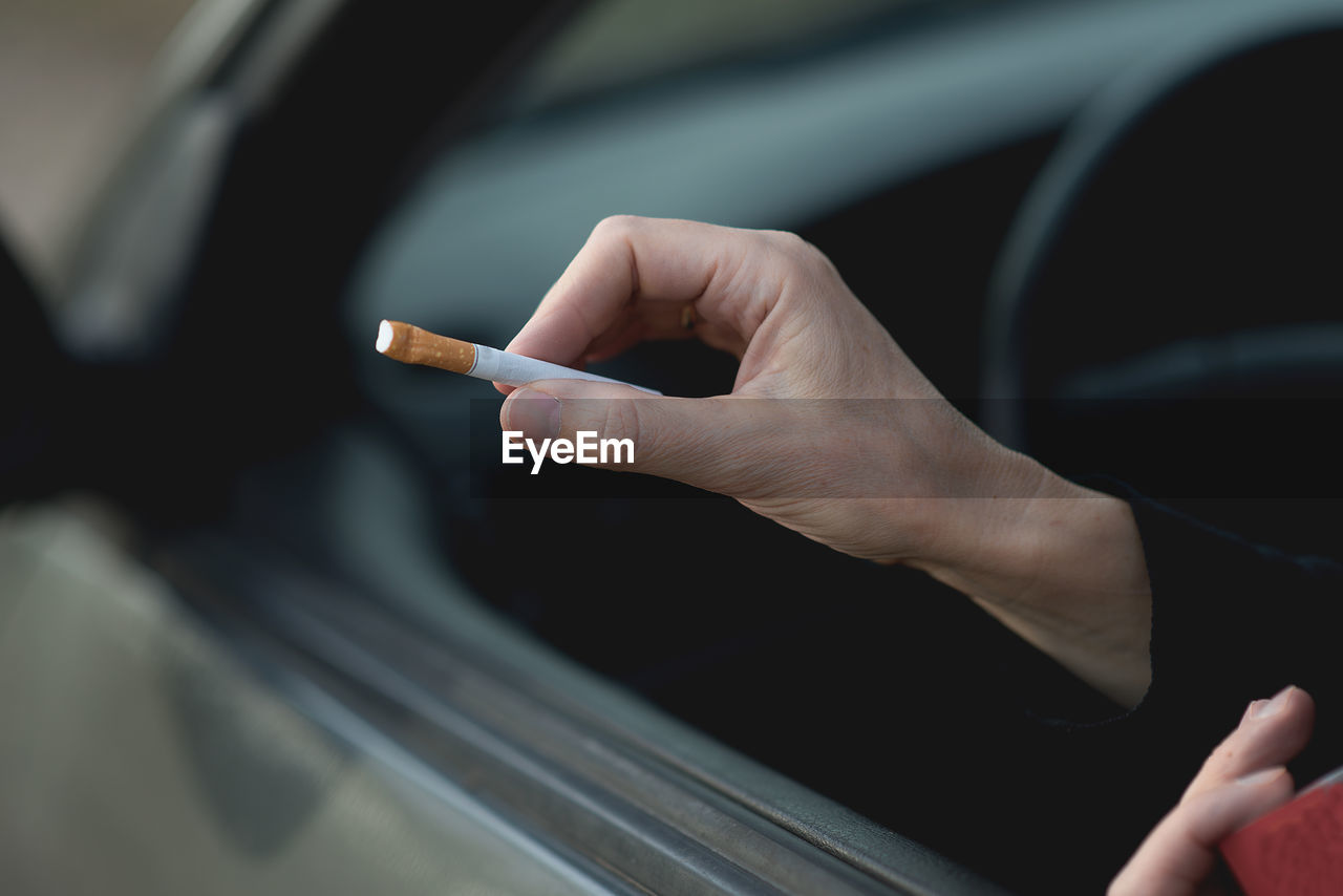 Cropped hand holding cigarette while sitting in car